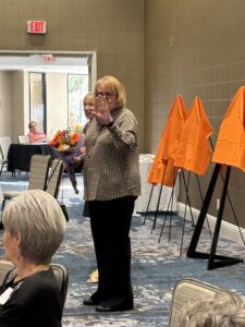 Woman waving at event, flowers and easels