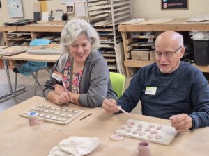 Two adults painting ceramic tiles at table