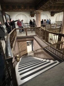 Visitors on balcony overlooking historic wooden staircase
