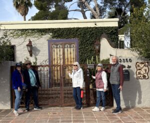 Five adults by ornate gate of stucco house